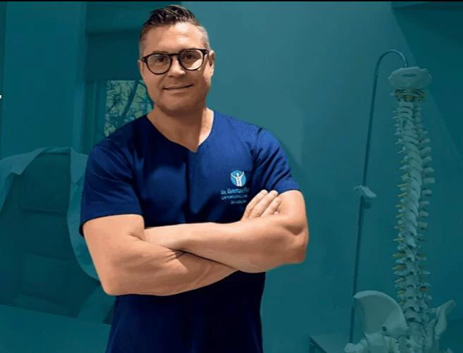 Dr. Everton Fiebig na clínica, ao lado de um modelo anatômico da coluna